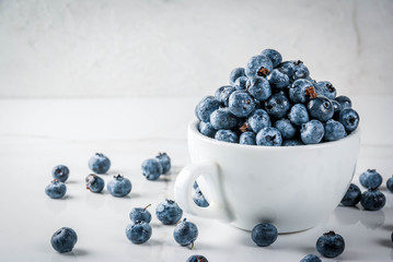 Fresh raw organic farm blueberry in white cup on white marble kitchen background, copy space