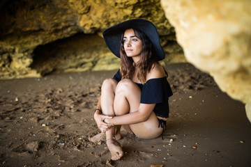 Happy beautiful latin woman wear in hat  sitting near on rocks beach on summer vocation time