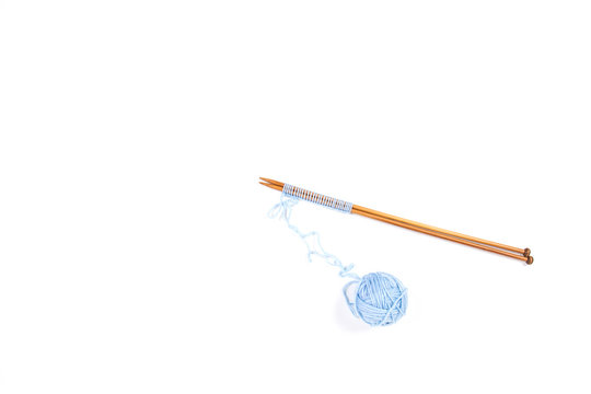 Knitting needles and blue yarn ball on white background