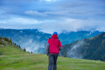 Fototapeta premium Traveler walks through the alpine meadow to the cliff