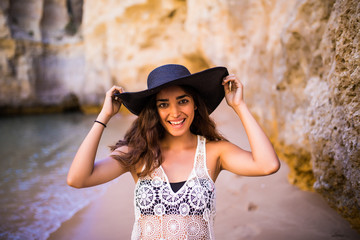 Portrait of beautiful latin girl on the beach with black hat smile neat ocean and rocks  on summer vocation