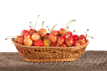 Yellow cherry in a wicker basket on a wooden table with a white background