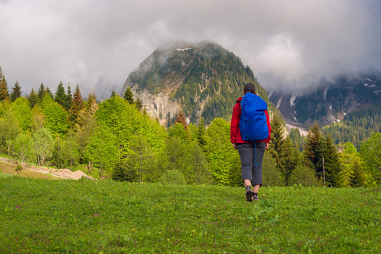 Woman traveler walk through the green meadow next to mountain range