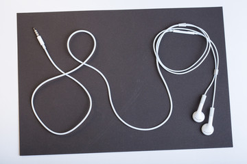 White headphones from your mobile phone on black background. Earphone wire twisted into a loop. Headphones for the gadget lying in the dark sheet