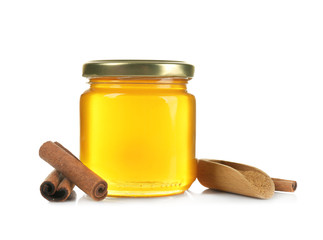 Jar with honey, cinnamon and wooden scoop on white background