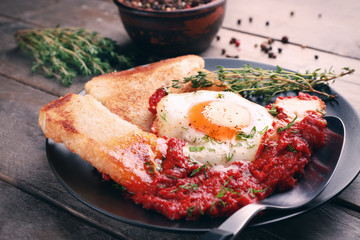 Plate with egg in purgatory on wooden background