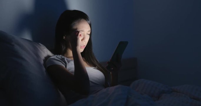 Woman feeling headache and using mobile phone on bed