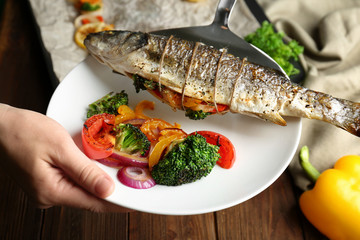 Woman putting baked fish on plate with vegetables