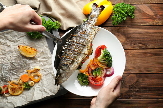 Woman putting baked fish on plate with vegetables
