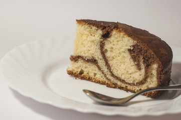 A piece of chocolate cake and a spoon on the saucer isolated on white background.