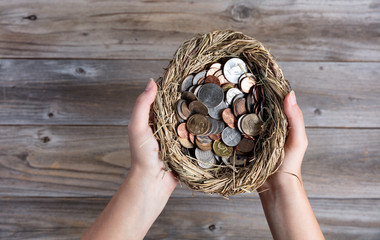 Hands holding nest egg filled with coins for savings concept