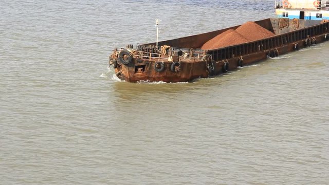Aerial clip of cargo barge transporting iron ore mined in hinterland to the main harbor for loading into big ships for exporting, along Zuari River in Goa, India