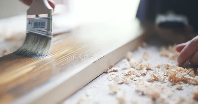 Young man painting wooden board with a brown paint.
