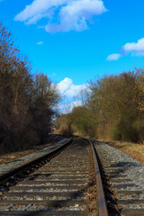 Obraz premium Bahnschiene zwischen Bäumen unter blauem Himmel