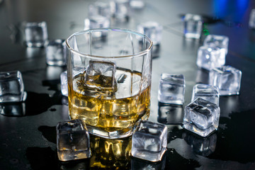 Close up whiskey in glass with ice cubes.dark black background.