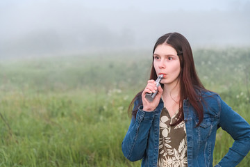 Girl is holding an electronic cigarette in her hand Concept smoking in public places. vaping. Summer