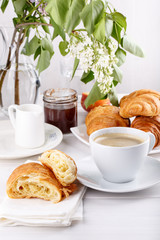 Breakfast - cup of coffee, croissants, jam and fruits on white table.