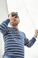 Naklejka premium man with beard looking through binoculars sailing yacht