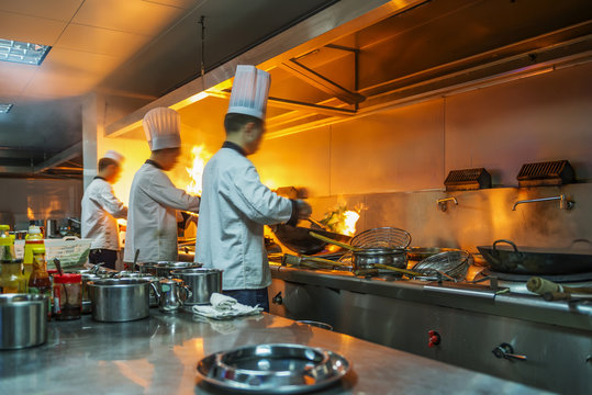 Chef in restaurant kitchen at stove with pan, doing flambe on food