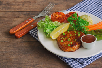 Barbecue pork steak on white plate served with barbecue sauce and vegetables. Pork steak for lunch or dinner on wood table. Moist and soft homemade pork barbecue served with mash potato and vegetable.