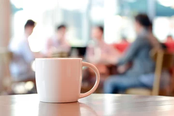 Poster Coffee cup on the table with people in coffee shop as blur background © Atstock Productions