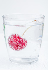 Ripe and sweet cherry in a glass of sparkling soda water placed on white background, healthy drinking concept.