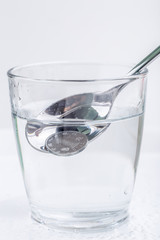 Japanese coin (yen) is picking up by silver spoon from a glass of water isolated on white background, financial concept.