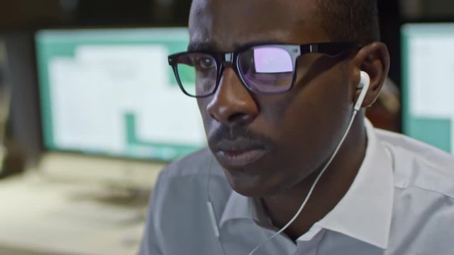 Closeup of black office worker listening to music with earphones and working on computer in the office at night