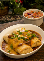 two chimichnga toppedwith chili gravy cheddar cheese greenn onions with aside of salsa