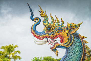 Fototapeta premium Naga Head Statue / Chiang Rai, Thailand - July 12, 2017: Naga Head Statue Inside Wat Rong Sua Ten Or Blue Temple At Rain Clouds Background.