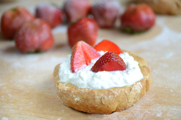 Muffin with fresh strawberries, white cream and powder on wooden brown board. Side view. Collection
