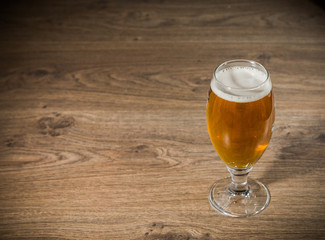 A glass of beer with foam on a wooden background