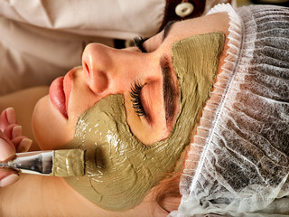 Mud facial mask of woman in spa salon. Massage with clay full face in therapy room. Healing clay to preserve youth.