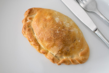Baked pasty on a white plate with knife and fork