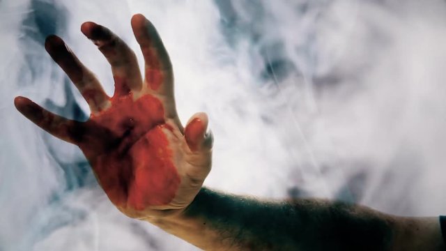 A smokey silhouette shot of a bleeding hand appearing and moving (searching for a victim to kill or eat). Horror, zombies, suspence, crime.
