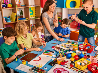 Fototapeta premium Plasticine modeling clay in children class. Teacher teaches kids together play dough and mold from plasticine in kindergarten or preschool. Preparation for exhibition of animals from plasticine.