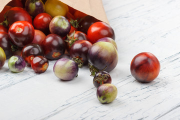 Different tomatoes in the paper bag on the white wooden background