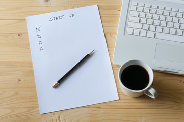 Paper check list for start up business laptop and coffee on wood table.