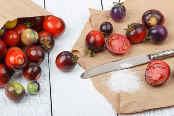 Different tomatoes in the paper bag on the white wooden background