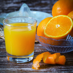 Close up of glass of freshly squeezed orange juice,  oranges fruit cut in half and glass citrus juicer on wooden table.