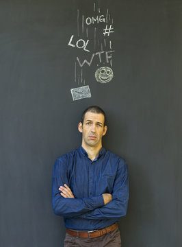 Single white adult man standing in front of a blackboard with drawn social media icons symbolizing frustration, stress and overload from modern communication