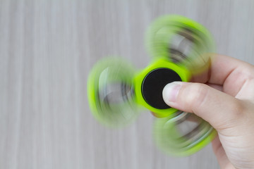A green hand spinner or fidget spinner is rotating in the girl's hand on the wooden background. A...