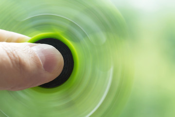 A green hand spinner or fidget spinner is rotating in the man's hand on the green background. A toy...