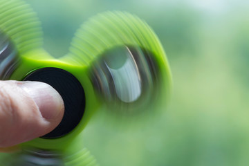 A green hand spinner or fidget spinner is rotating in the man's hand on the green background. A toy for stress relieving. Close up. Selective focus.