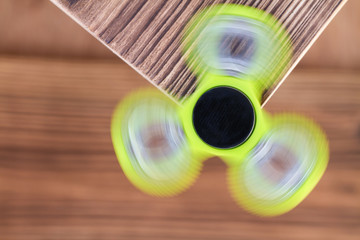 A green hand spinner or fidget spinner is rotating on wooden background. A toy for stress...
