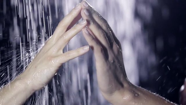 under the streams of running water in the shower. a contact between two graceful palms fingers. close-up
