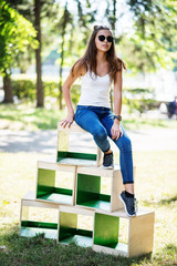 Portrait of a fashionably dressed girl posing on wooden boxes in the park on a sunny day