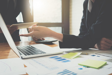 Business woman discussing something and showing data with her laptop computer to her coworker while using tablet and calculator