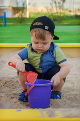 Charming cute boy playing in the sandbox on the playground