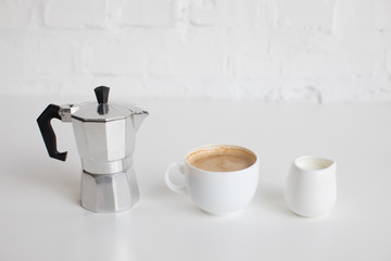 french press, cup of coffee and milk jar standing in row on white table